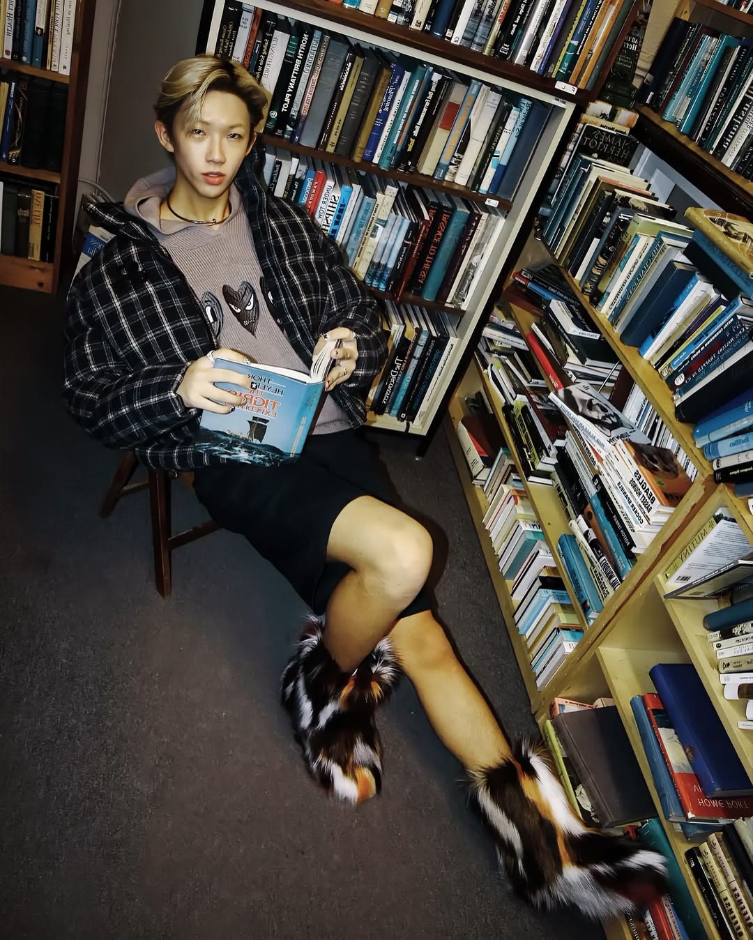Fashion portrait seated with an open book between tightly packed shelves