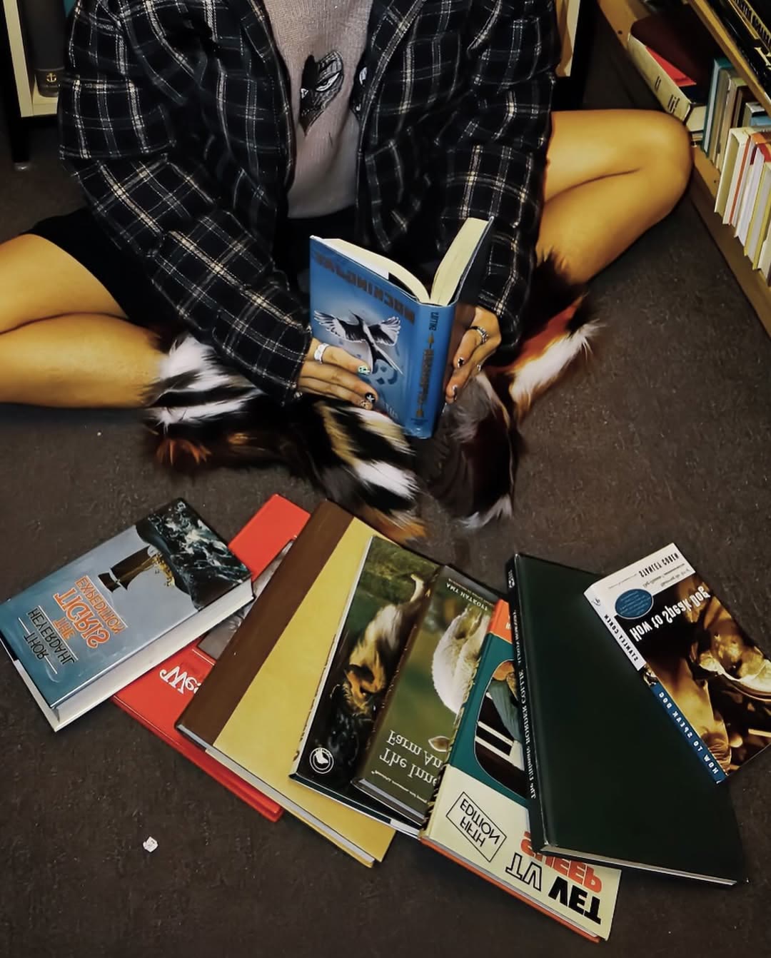 Hands holding an open book among patterned clothing and scattered book covers